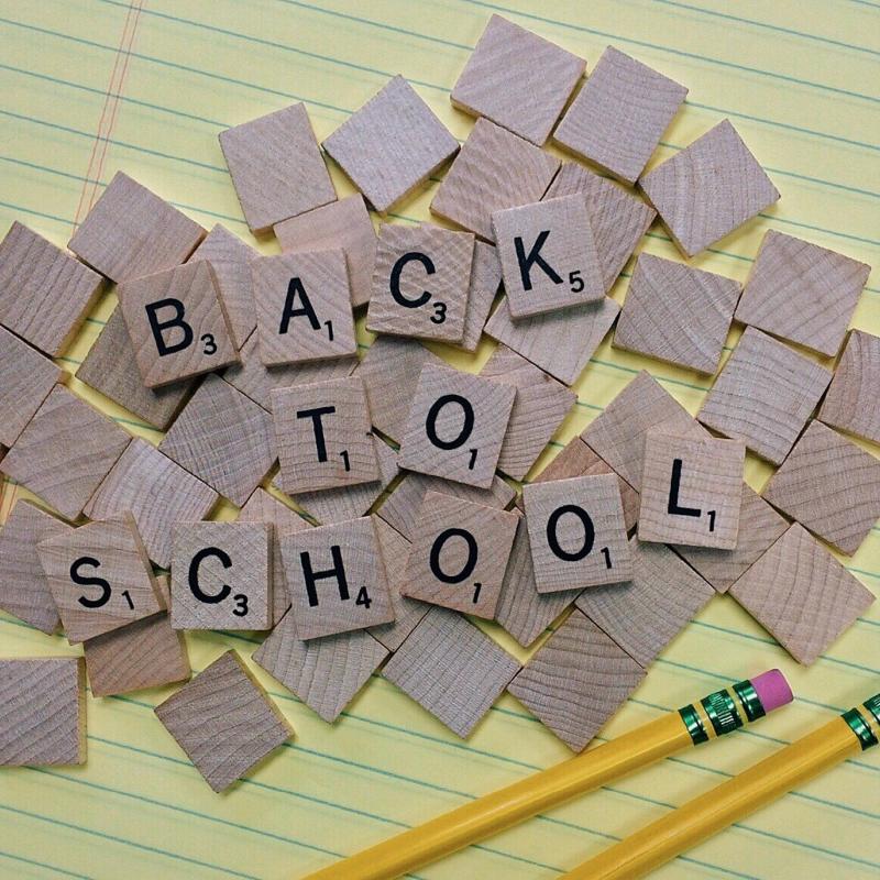 wooden scrabble tiles spelling Back To School on yellow lined paper with two pencils